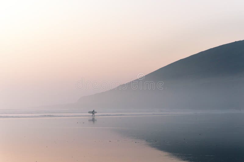 En ensam surfare som promenerar stranden på en dimmig vintereftermiddag Saunton Devon, UK arkivfoto En ensam surfare som promenerar stranden på en dimmig vintereftermiddag Saunton Devon, UK arkivfoto