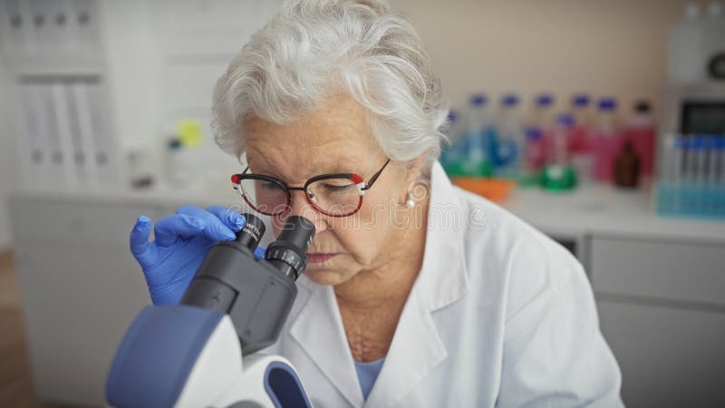 En erfaren kvinnlig forskare undersöker prover genom ett mikroskop i ett modernt laboratorium royaltyfri fotografi
