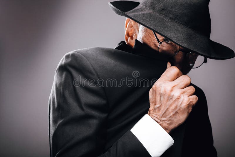 En gammal manlig skådespelare som spelar en enastående spionroll och gömmer sig bakom fedora hat. royaltyfria bilder