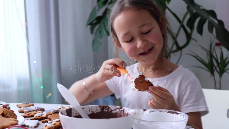 En glad flicka dansar och sjunger medan man dekorerar kakor med isbildning