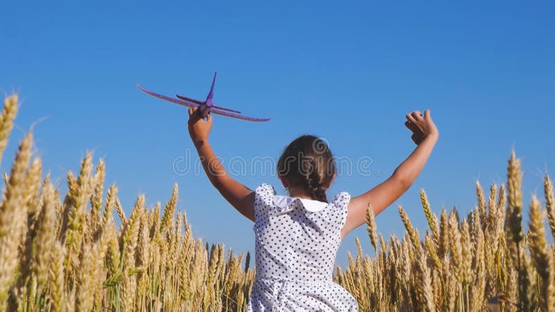 En glad flicka flyger med ett leksaksflygplan på ett vetefält under blå himmel. barn spelar leksaksflygplan. tonåringars drömmar o