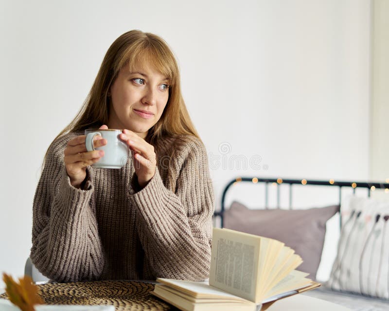Smiling beautiful female drinking cup of tea and reading book in bedroom interior. Happy woman spending daytime without gadgets and social media. Slow living lifestyle. Enjoy moment. Smiling beautiful female drinking cup of tea and reading book in bedroom interior. Happy woman spending daytime without gadgets and social media. Slow living lifestyle. Enjoy moment
