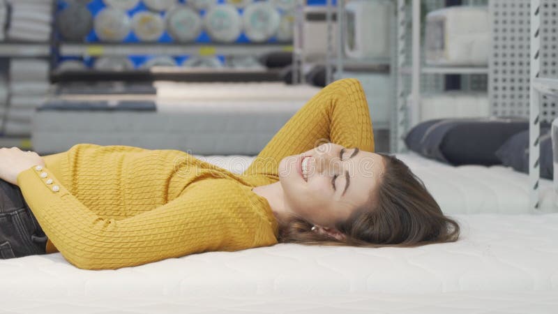 En glad ung kvinna som roar sig med nya madrasser i möbelbutiken