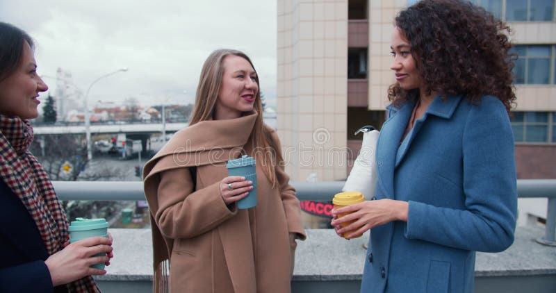 En glad, vacker, multietnisk, ung företagskvinna gillar att prata med kaffe från ekobungar utanför på kall höstdag. arkivfilmer