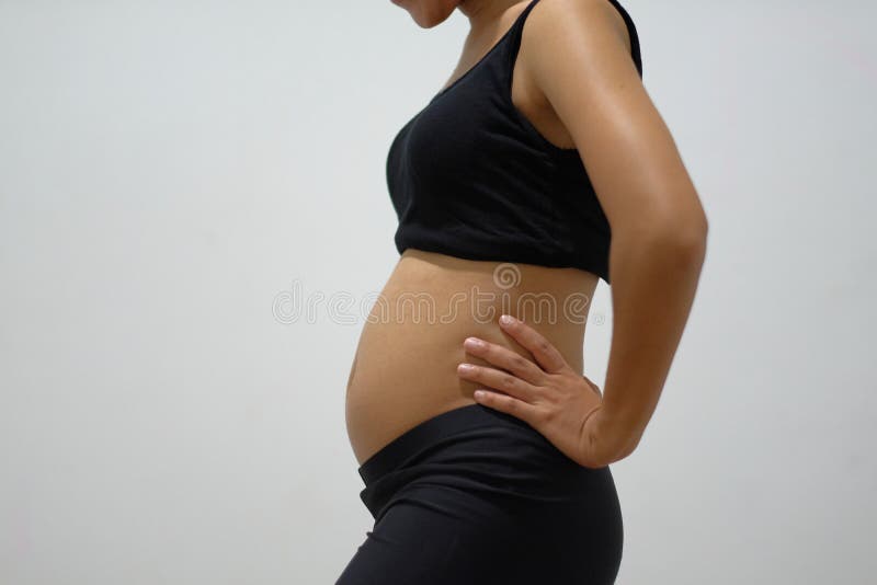 a pregnant woman aged 3 months wearing a black tank top and her hands supporting her waist in front of a white wall. a pregnant woman aged 3 months wearing a black tank top and her hands supporting her waist in front of a white wall