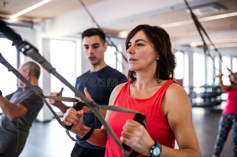 En grupp av gladlynta pensionärer i idrottshall med en ung instruktör som gör övning med TRX arkivfoto En grupp av gladlynta pensionärer i idrottshall med en ung instruktör som gör övning med TRX arkivfoto