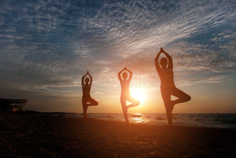 En grupp av kvinnor som gör yoga på soluppgång nära havet arkivfoton En grupp av kvinnor som gör yoga på soluppgång nära havet arkivfoton