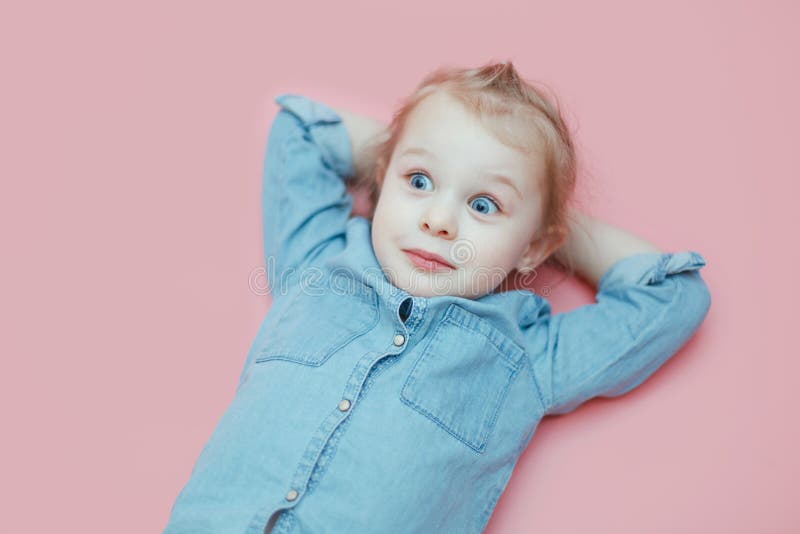 En gullig vit liten flicka ligger på en rosa bakgrund med hennes händer bak hennes huvud fotografering för bildbyråer En gullig vit liten flicka ligger på en rosa bakgrund med hennes händer bak hennes huvud fotografering för bildbyråer