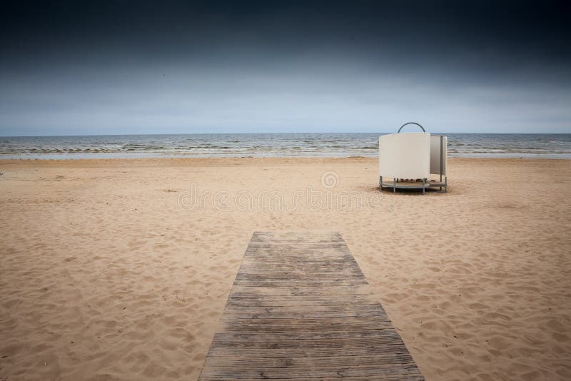 En gångväg av trä leder till en tom baltisk strand vid Jurmala Lettland, blek sand skonsam surf och en ensam växlingsplats i kabin arkivfoto