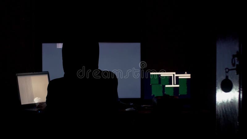 En hacker i huv som knäcker kod genom att använda datorer i mörkt rum