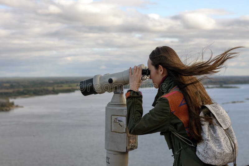 En handelsresande för ung kvinna på observationsdäcket som ser till och med kikare på panoraman av staden av Nizhny Novgorod arkivbilder En handelsresande för ung kvinna på observationsdäcket som ser till och med kikare på panoraman av staden av Nizhny Novgorod arkivbilder