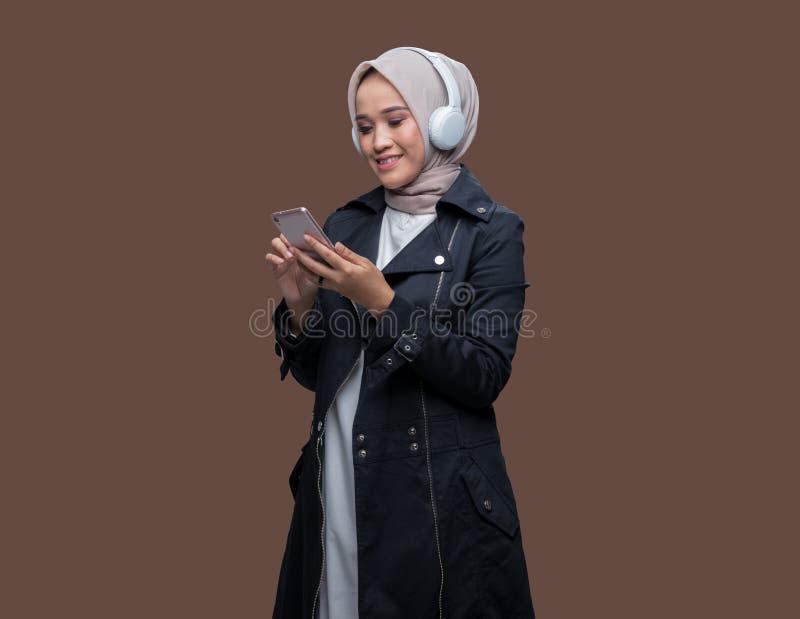 En hijab-kvinna som bar hörlurar rörde på sin mobilskärm arkivfoton