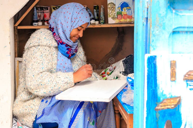 En härlig marockansk flicka, ett muslimskt, gatakonstnär målar en bild med en borste i ett litet seminarium royaltyfri bild En härlig marockansk flicka, ett muslimskt, gatakonstnär målar en bild med en borste i ett litet seminarium royaltyfri bild