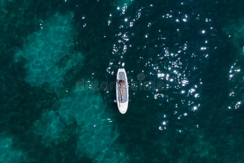 En härlig ung kvinna kopplar av på ett SUPbräde i havet nära ön Surrskott arkivbild En härlig ung kvinna kopplar av på ett SUPbräde i havet nära ön Surrskott arkivbild