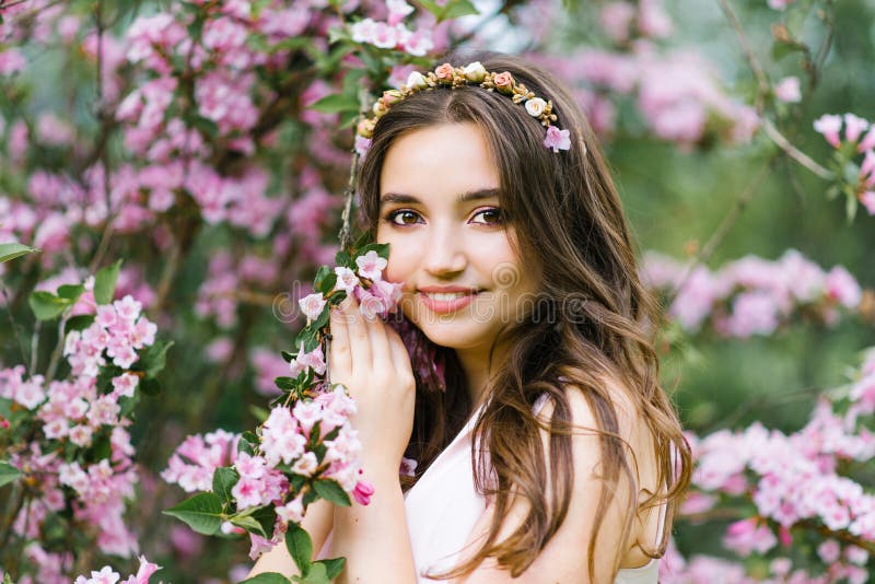 En härlig ung nätt flicka med långt hår lossar ställningar nära den blommande våren Bush av weigelaen med rosa blommor Hon trycke arkivfoton En härlig ung nätt flicka med långt hår lossar ställningar nära den blommande våren Bush av weigelaen med rosa blommor Hon trycke arkivfoton