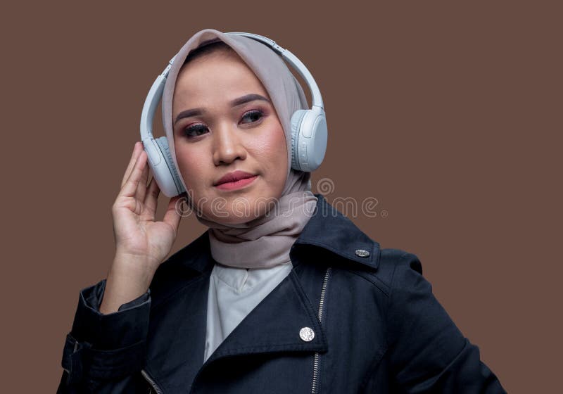 En indonesisk hijab-kvinna som lyssnar musik med hjälp av trådlösa hörlurar med ett allvarligt uttryck royaltyfri bild