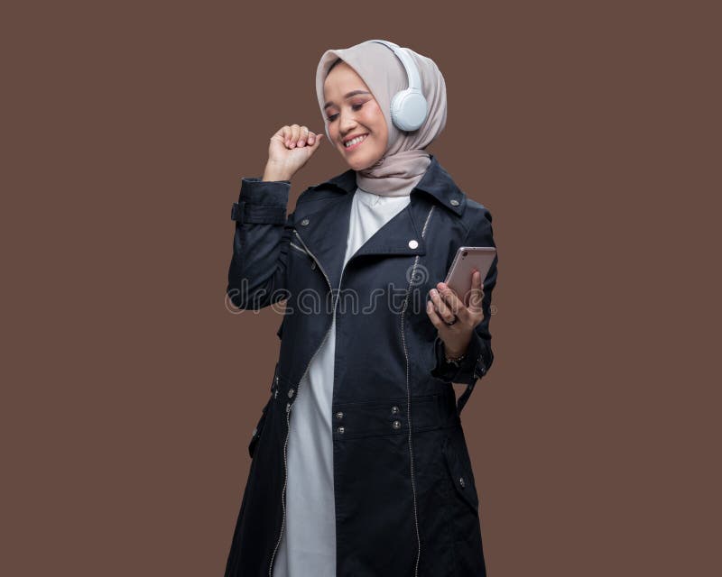 En indonesisk kvinna i hijab lyssnar på musik från sin mobiltelefon med trådlösa hörlurar medan hon dansar arkivfoto