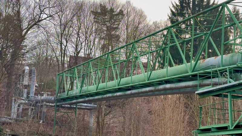 En industribro med en grön rörledning som flödar genom Lush Trees nära strukturen royaltyfri bild