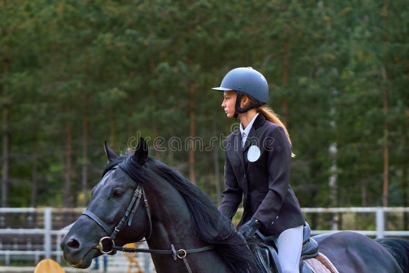 En jockey för ung kvinna på en häst utför ett hopp över barriären arkivbild