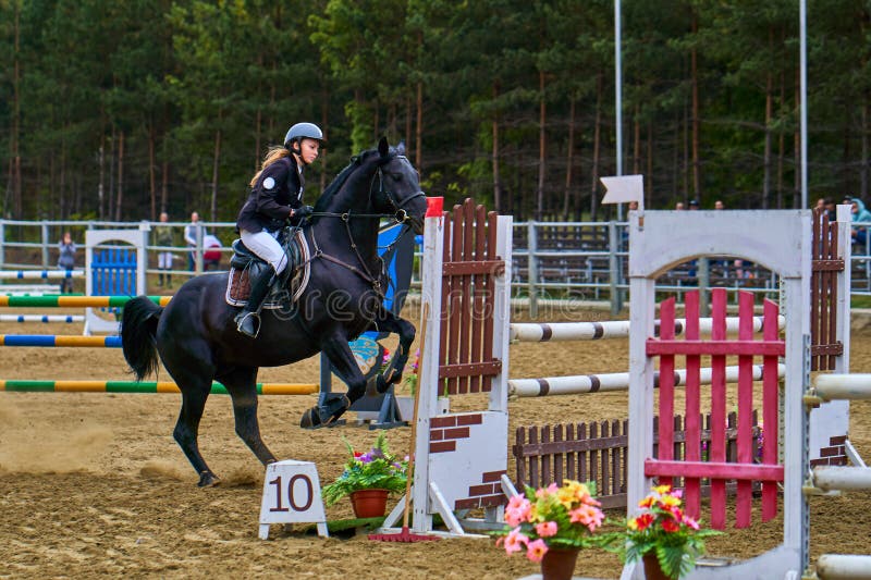 En jockey för ung kvinna på en häst utför ett hopp över barriären royaltyfria foton
