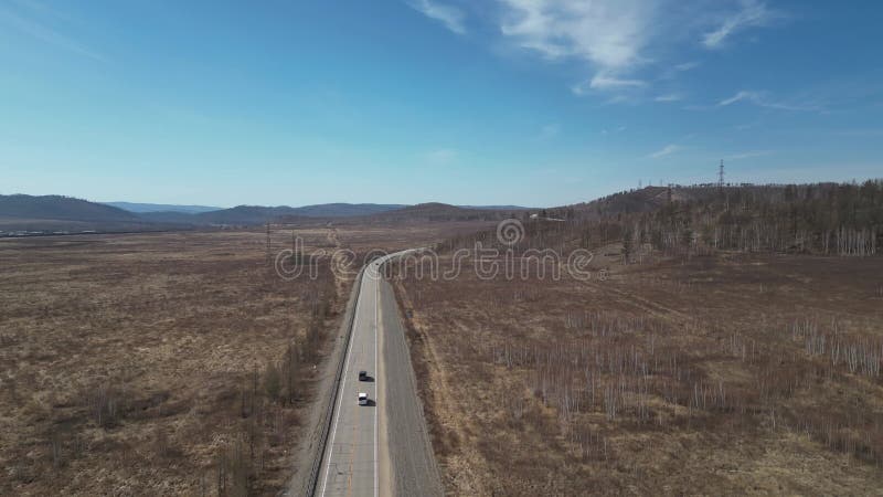 En kamera följer efter två bilar som kör längs en väg i stäppen en solig dag stock video