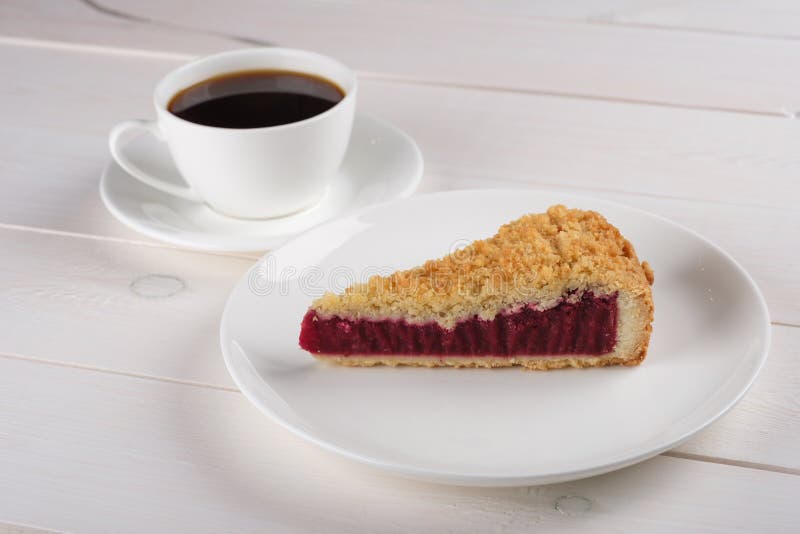 En kopp av svart kaffe och ett stycke av bärpajen på en platta står på en vit trätabell arkivbild En kopp av svart kaffe och ett stycke av bärpajen på en platta står på en vit trätabell arkivbild