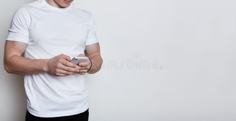 En kropp av smartphonen för vit T-tröja för muskulös pojke som den bärande hållande skriver ett meddelande som direktanslutet med arkivfoto En kropp av smartphonen för vit T-tröja för muskulös pojke som den bärande hållande skriver ett meddelande som direktanslutet med arkivfoto