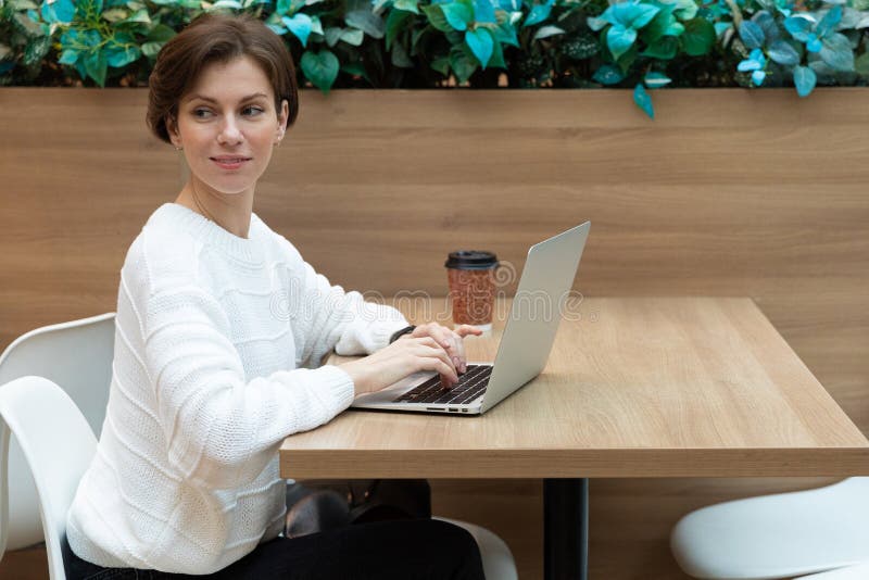 En kvinna i ett kafé väntar på en affärspartner som sitter på en bärbar dator arkivfoto