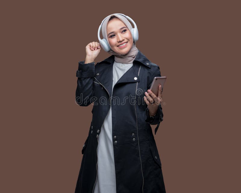 En kvinna i hijab lyssnar på musik från sin mobiltelefon med trådlösa hörlurar medan hon dansar arkivfoto