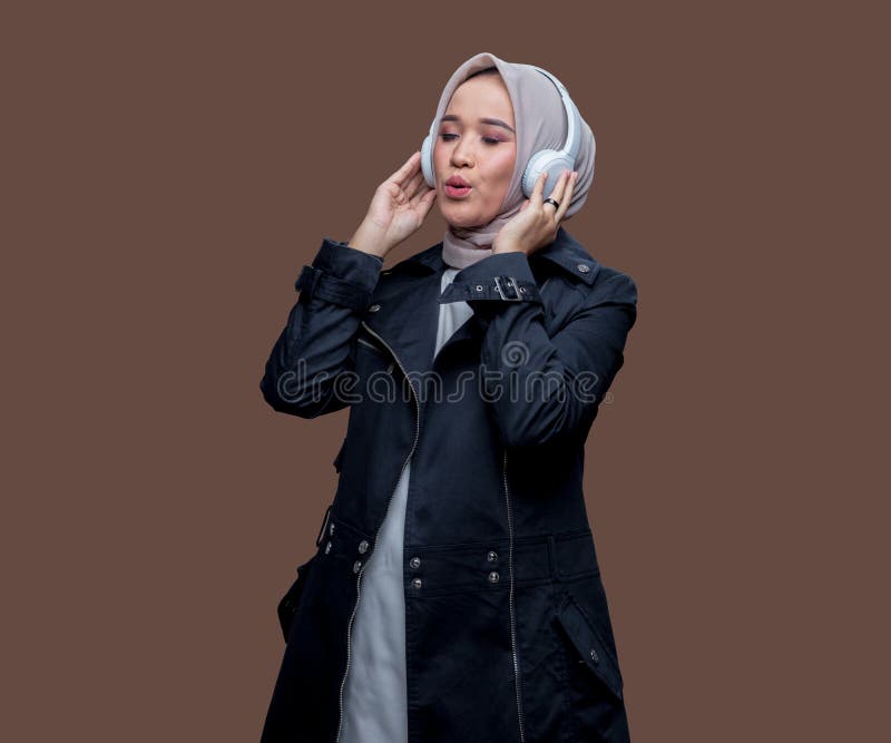 En kvinna i hijab som har trådlös hörlurar medan hon piskar och blundar fotografering för bildbyråer
