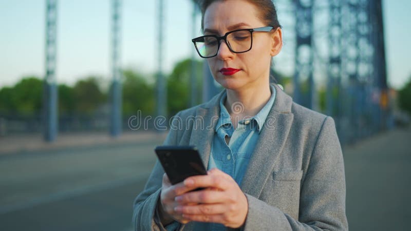 En kvinna i en rock som går runt i stan tidigt på morgonen med smartphone