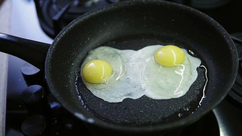 En kvinna knäcker nya ägg i en stekpanna med varmt och att fräsa smör Sen frukost efter dusch Saltade och att förbereda sig