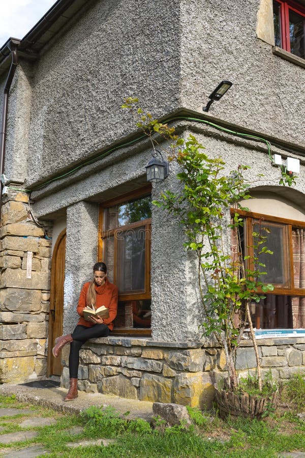 Woman with crossed legs reading at the entrance of a country house, vertical. Woman with crossed legs reading at the entrance of a country house, vertical