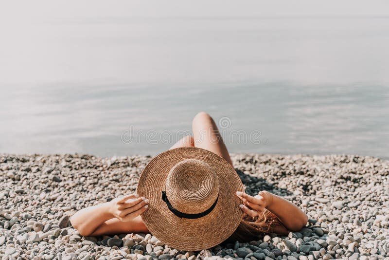 En kvinna på stranden som bär halmhatt. Hon är avslappnad och njuter av solen. royaltyfri foto