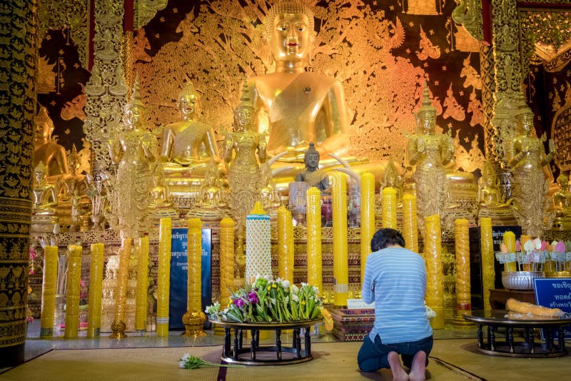 En kvinna sitter för att be framme av den guld- Buddhastatyn av Thailand templet namngav ’Wat Den Salee Sri Muang Gan Wat Ban Den arkivbilder En kvinna sitter för att be framme av den guld- Buddhastatyn av Thailand templet namngav ’Wat Den Salee Sri Muang Gan Wat Ban Den arkivbilder