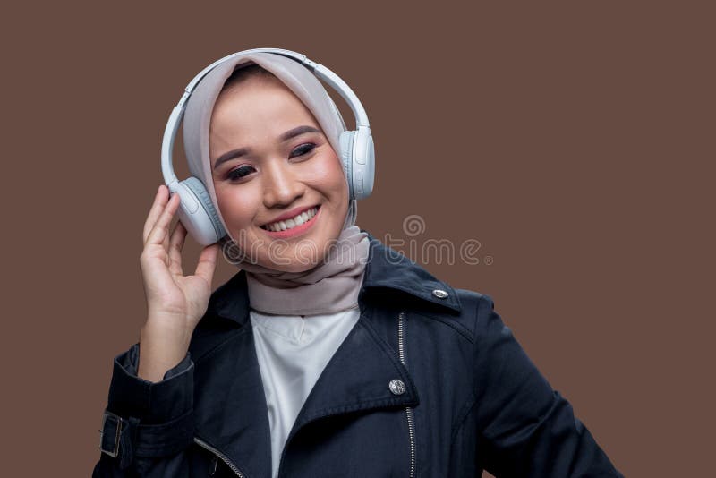 En kvinna som bar hijab lyssnade på musik med hjälp av trådlösa hörlurar med ett leende uttryck arkivbilder
