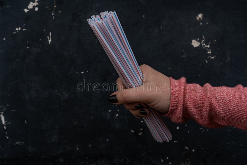 Woman holds a punch of plastic straws with one hand I a black sworn background. Woman holds a punch of plastic straws with one hand I a black sworn background.