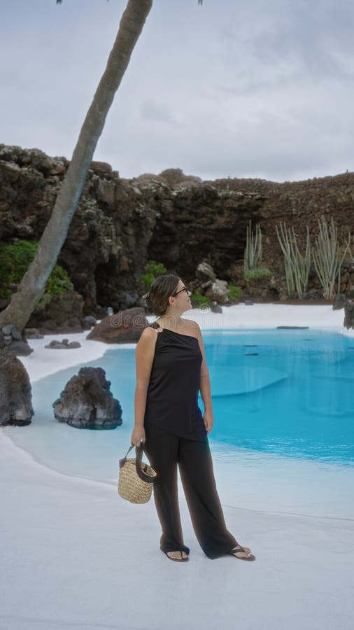 En kvinna som står framför en turkospool vid jameos del agua lanzarote-kanarieöarna och bär svarta kläder och ett fotografering för bildbyråer