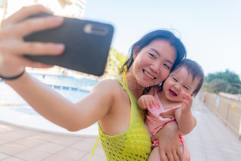 En kvinna som tar självfotografi med sin vackra flicka, vackra kinesiska mor som håller sin lilla dotter och tar med sig sin lilla fotografering för bildbyråer