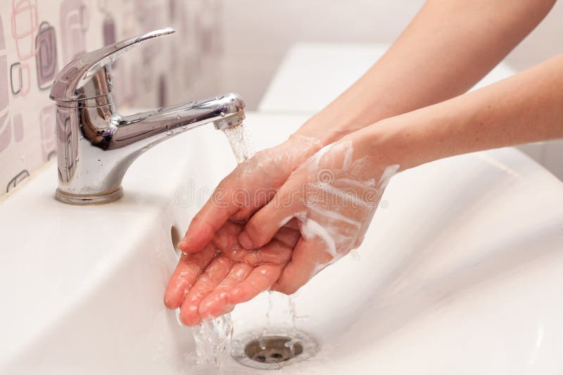 En kvinna tvättar tvålskum från hennes händer under rinnande vatten hygien Tvättande händer i badrummet