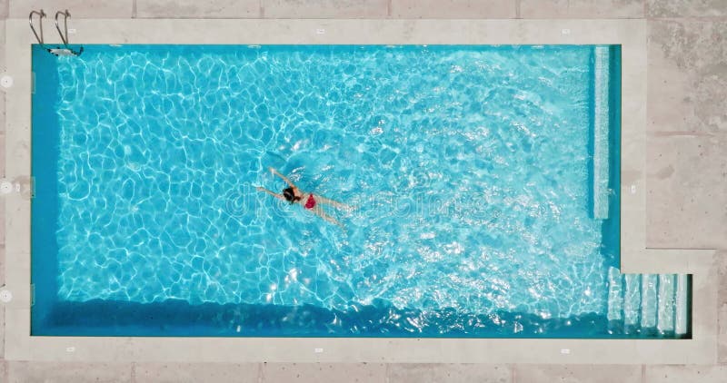 En kvinnas flygsyn i en röd baddräkt som simmar i poolen. Sommarlivsstil