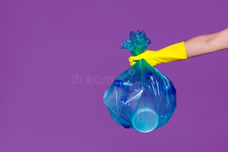 En kvinnas hand i en gummihandske rymmer en genomskinlig blå avskrädepåse med tomma plast- flaskor royaltyfri foto En kvinnas hand i en gummihandske rymmer en genomskinlig blå avskrädepåse med tomma plast- flaskor royaltyfri foto