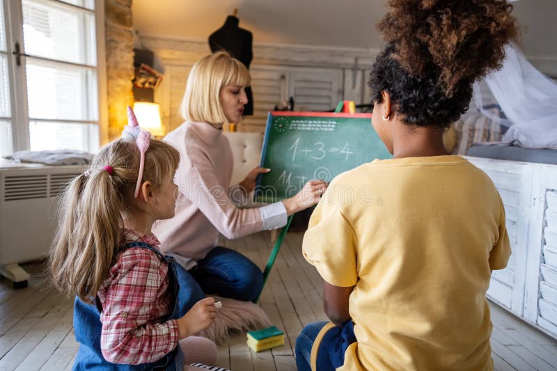 En kvinnlig lärarmamma som visar nya matematikuppgifter för elementära, mångskiftande skolbarn arkivfoto