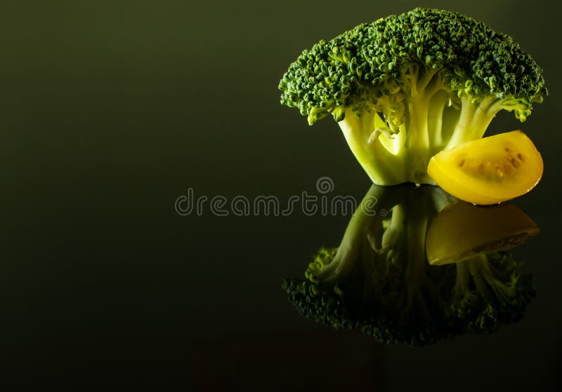 En kvist av broccoli med en skiva av den gula körsbärsröda tomaten royaltyfria bilder En kvist av broccoli med en skiva av den gula körsbärsröda tomaten royaltyfria bilder