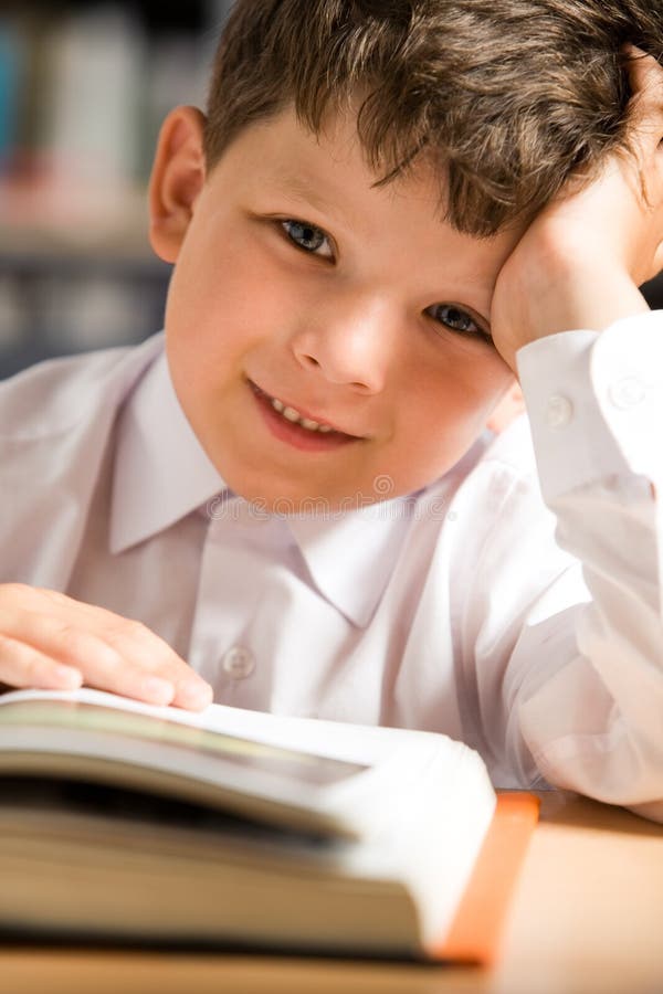 Close-up of smiling schoolkid touching page of open book and looking at camera with positive expression. Close-up of smiling schoolkid touching page of open book and looking at camera with positive expression