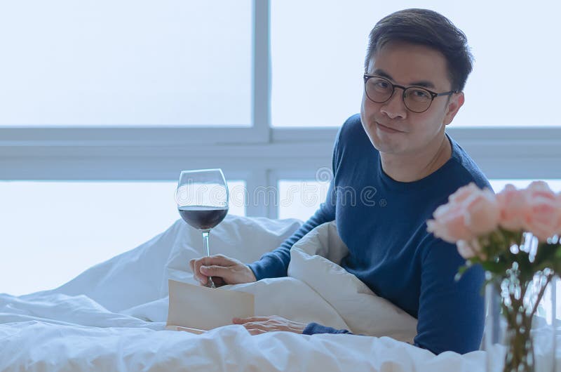 A smiling person that reading book on bed with a glass of red wine. Good mental health concept. A smiling person that reading book on bed with a glass of red wine. Good mental health concept