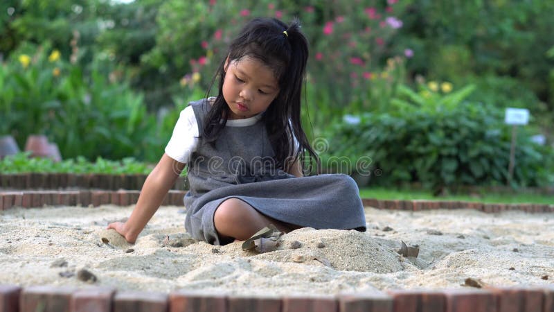 En liten asiatflicka som sitter i sandlådan och spelar en leksakshovelbucket och hon sparkade i en leksakshovelbucket.. spel