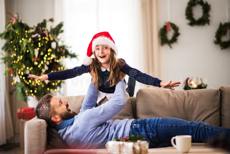 En liten flicka med jultomtenhatten som spelar med hennes fader som är hemmastadd på jultid royaltyfria foton En liten flicka med jultomtenhatten som spelar med hennes fader som är hemmastadd på jultid royaltyfria foton