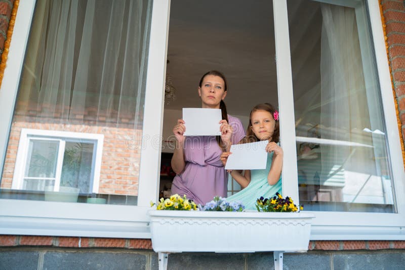 En liten flicka med moderkvinna från fönstret visar ett tomt blad för ett meddelande royaltyfri foto