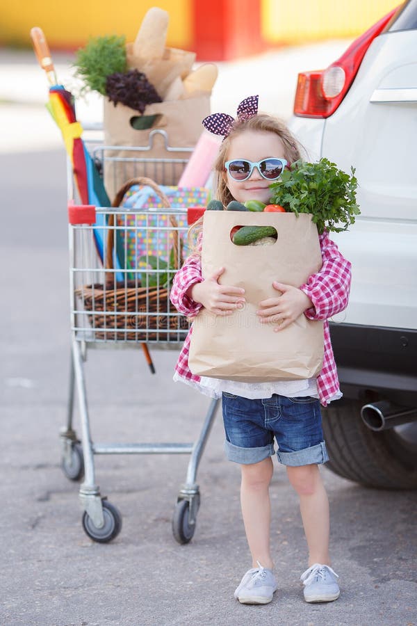 En liten flicka med stor vagn köper färsk mat och färska grönsaker i en stor stormarknad bara under sommaren.